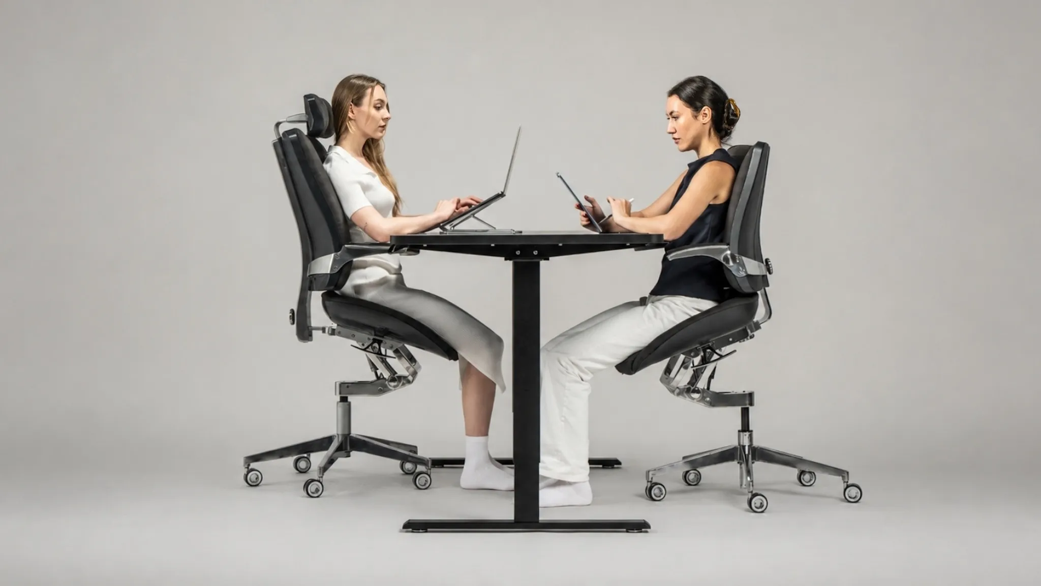 Two professionals work comfortably across a shared desk while seated in Levitask Vision ergonomic chairs.