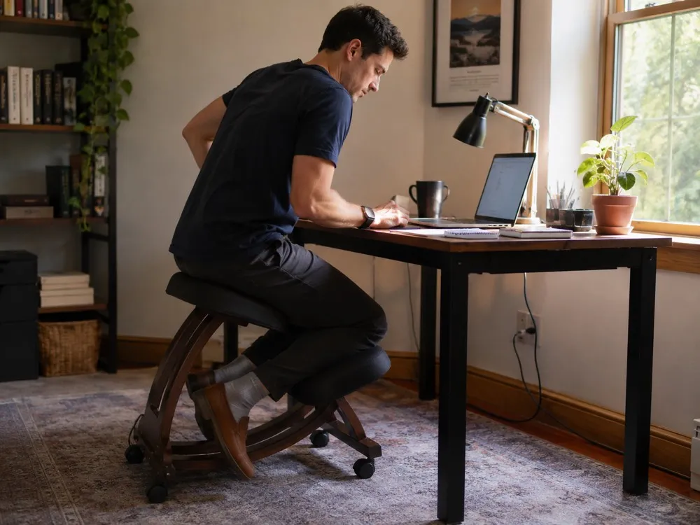 Side illustration of a kneeling chair showing the forward seat slope, open hip angle and weight shared between seat and shins.